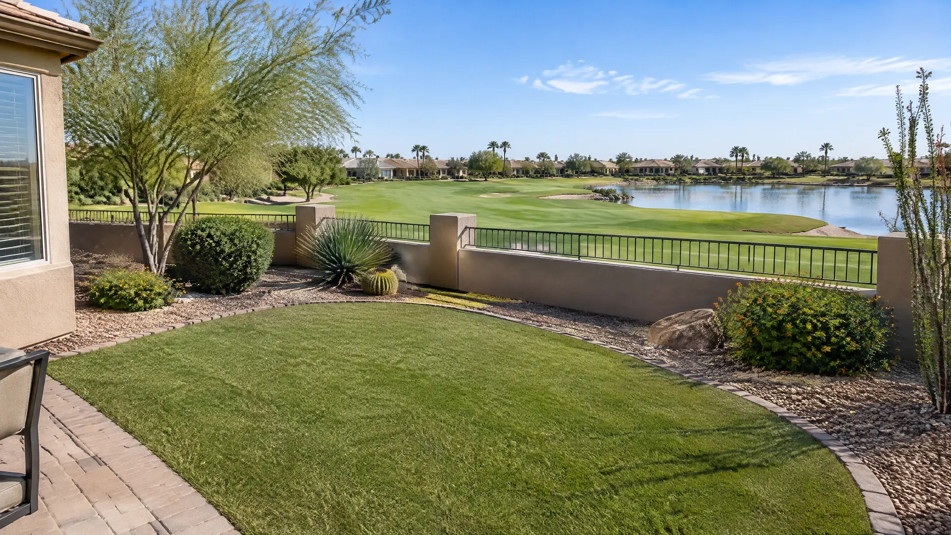 Small low-maintenance backyard of a single-story home in a 55-plus golf community in south Chandler, Arizona: a neat patch of artificial turf, gravel and a few desert plants, a low wall opening to a golf fairway and a lake beyond
