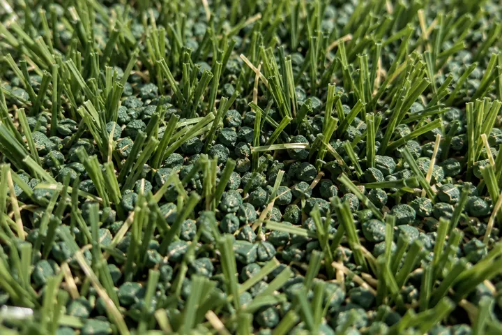Close-up of greenish antimicrobial-style infill granules scattered between short artificial grass blades