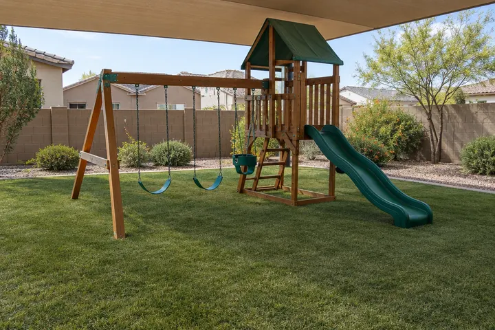 Synthetic turf lawn under a shaded play area with a wooden swing set in a family backyard, no children present